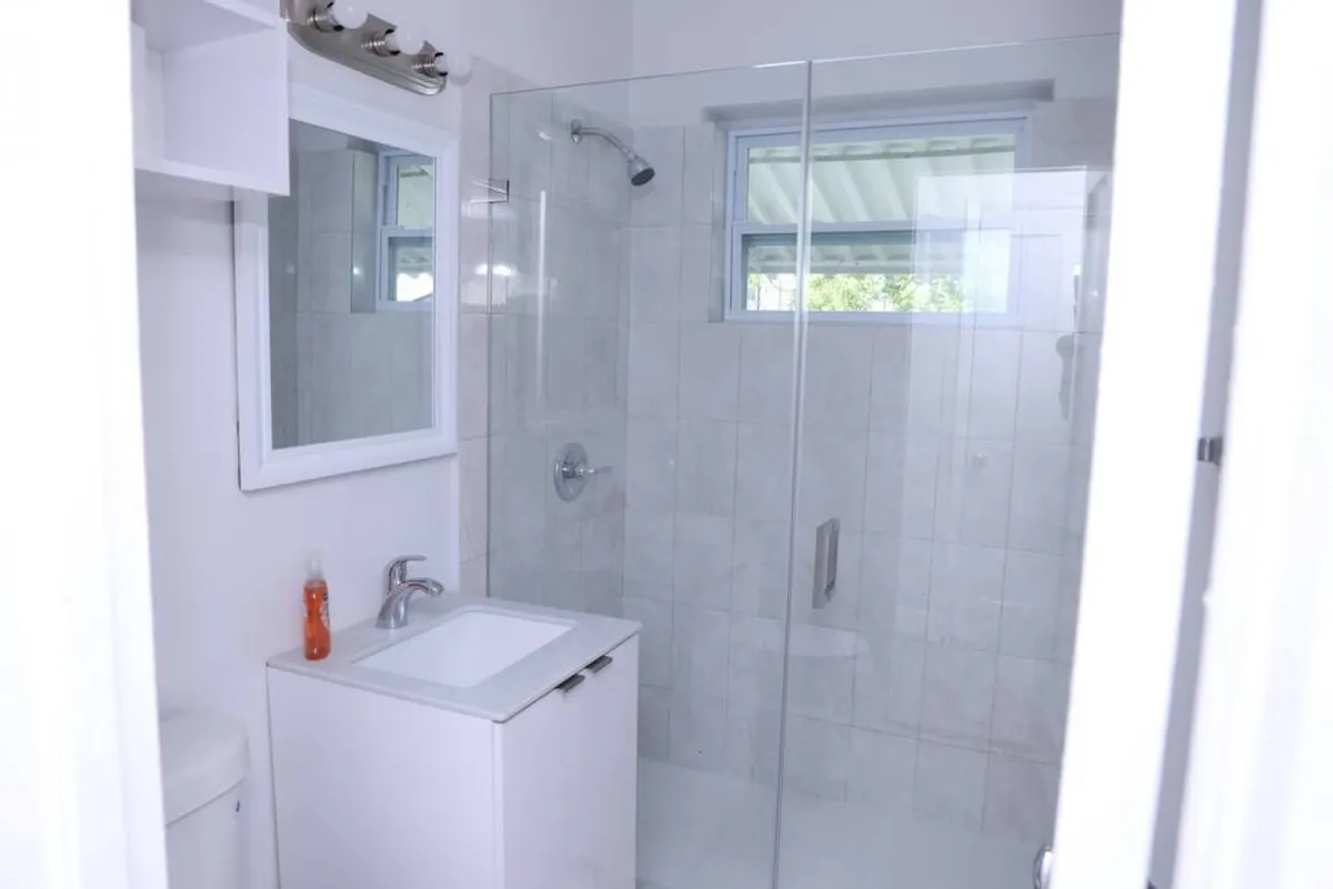 This image shows a modern bathroom interior with a glass shower enclosure, a vanity with sink, and a large mirror. The space is designed for personal grooming and self-care routines, with a clean, refreshing, and relaxing atmosphere.