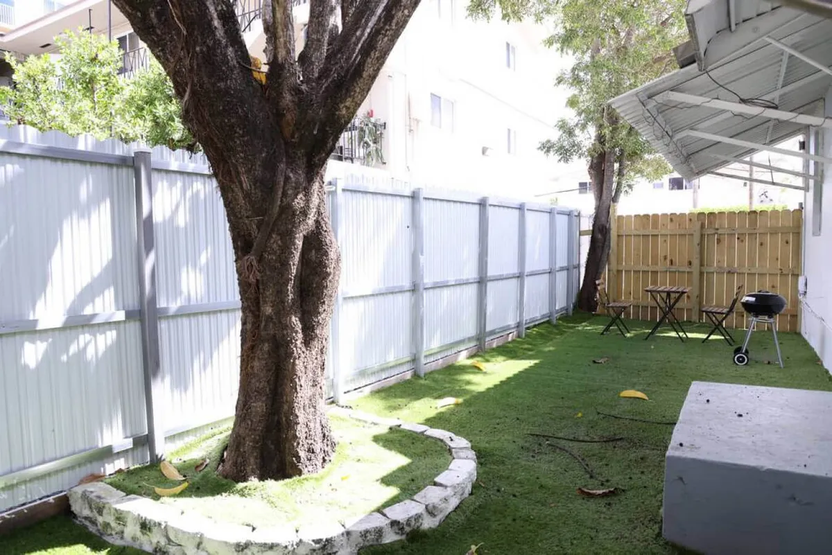 This image focuses on the private outdoor seating area shaded by a large tree, with a grill in the backdrop. The relaxed setup is ideal for sunset dinners, daytime picnics, or stargazing, emphasizing the property's outdoor living and entertaining potential.